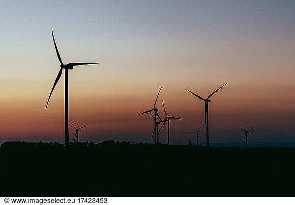 Silhouettes of wind turbines standing against moody sky at dusk