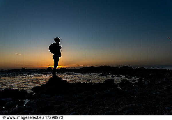 Silhouettierte Figur am felsigen Ufer mit Sonnenuntergang Himmel hinter