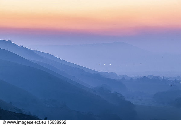 Silhouettierte Hügellagen und ein farbenfroher Sonnenuntergang durch Nebel im South Downs National Park; Brighton  East Sussex  England