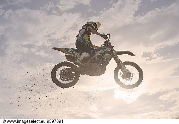 Silhouettierter junger  männlicher Motocross-Rennfahrer  der in der Luft springt.