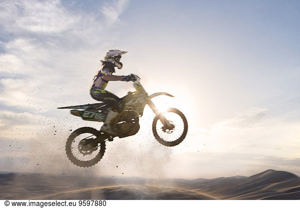Silhouettierter junger  männlicher Motocrosser  der über die Schlammbahn springt.