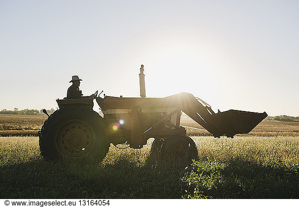 Silhouettierter älterer männlicher Landwirt mit Traktor auf dem Feld  Plattsburg  Missouri  USA