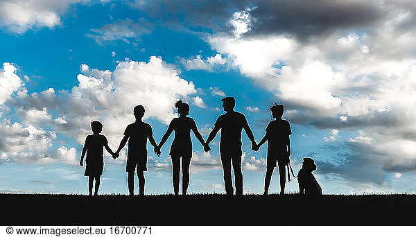 Silhoutte of a family of five with their dog against a cloudy sky.