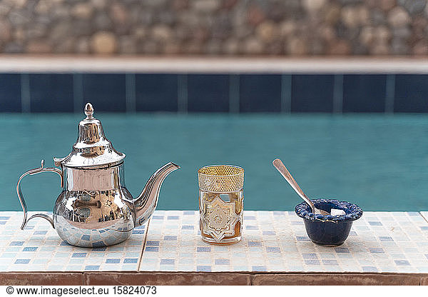 Silver tea pot  tea glass and sugar bowl on poolside
