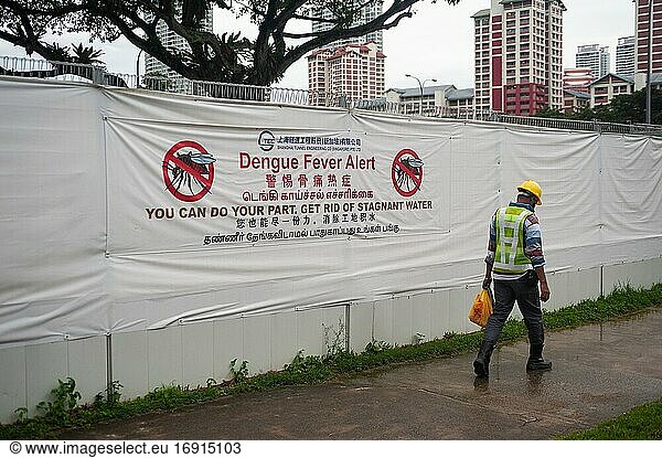 Singapur  Republik Singapur  Asien - Ein Arbeiter geht an einer Baustelle in einem Wohngebiet vorbei  an der ein riesiges Banner angebracht ist  das vor der Ausbreitung von Dengue-Fieber-Infektionen durch Mücken warnt  da diese das auf Baustellen vorkommende stehende Wasser als potenziellen Brutplatz nutzen.