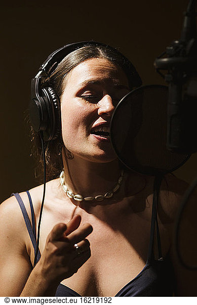 Singer with headphones at microphone in recording studio