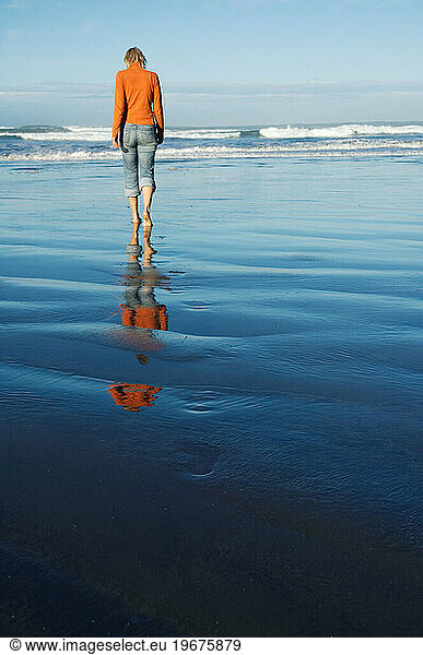 Single alone female walking along sea shore of empty west coast beach  New Zealand