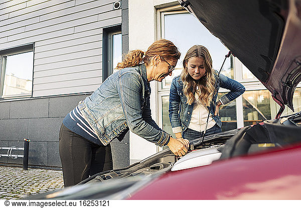 Single mother repairing car while daughter standing at roadside