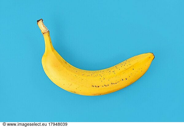 Single ripe banana with peel on blue background