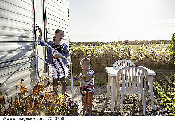 Sister (4-5) and brother (18-23 months) outside caravan in field