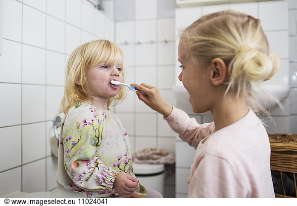 Sister brushing girls teeth while standing in bathroom