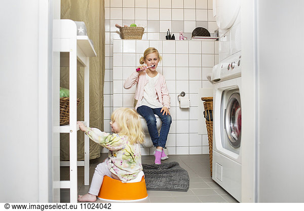 Sister looking at girl sitting on potty trainer