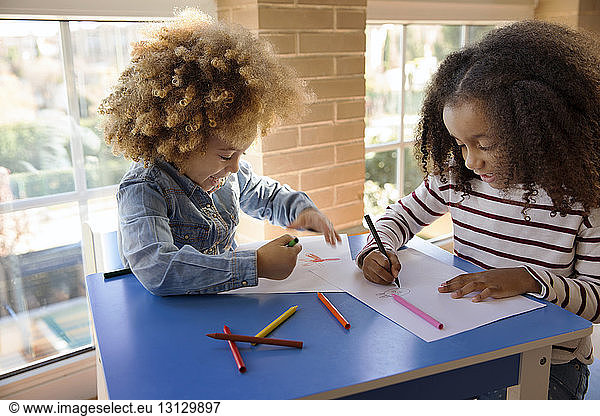 Sisters drawing on papers at table