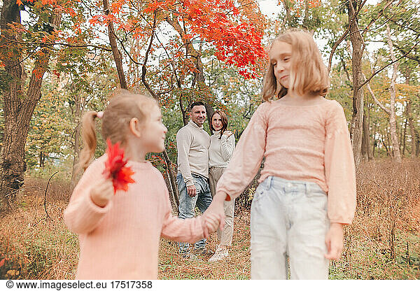 Sisters Holding Hands on the Background of Parents in the Park