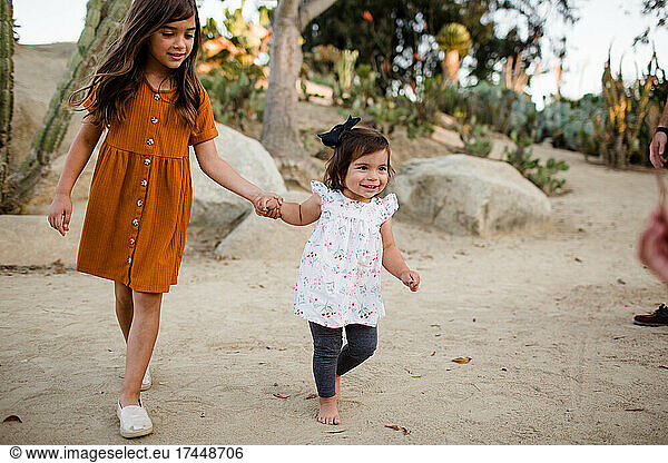 Sisters Holding Hands & Walking Through Desert Garden in San Diego
