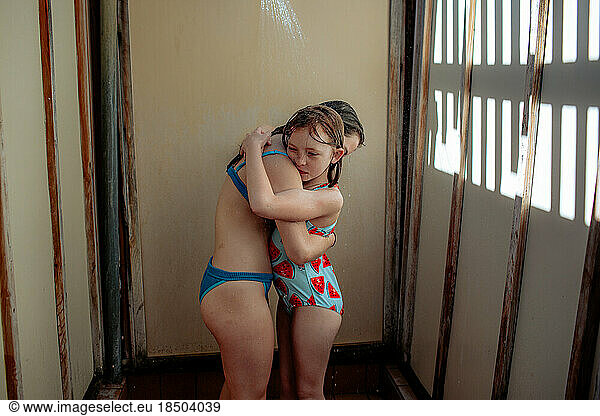 Sisters hugging in outdoor shower after swimming
