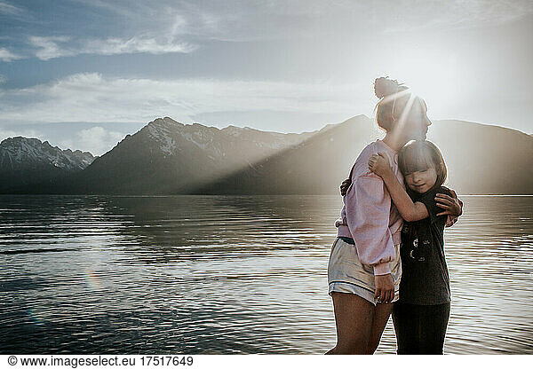 Sisters hugging near alpine lake on a sunny day