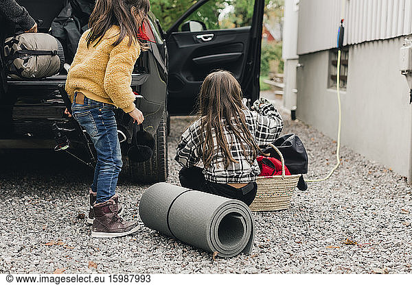 Sisters loading luggage in electric car trunk while going for picnic