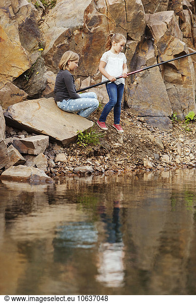 Sisters on rocks fishing in lake