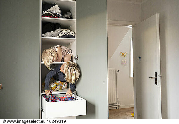 Sisters sitting on shelves in wardrobe