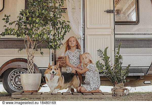 Sisters sitting with corgi dog at doorway of camper van