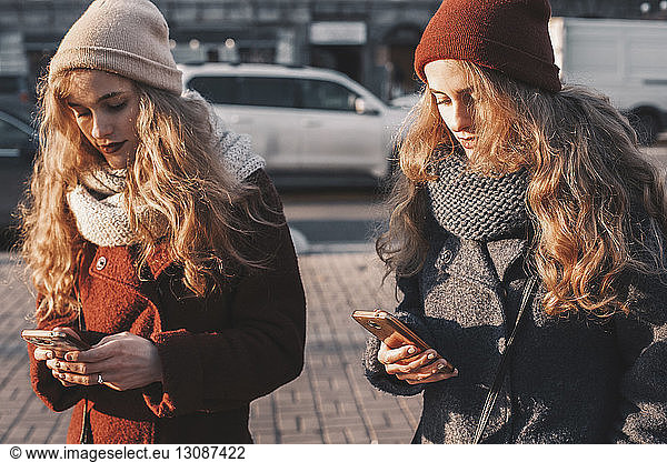 Sisters using mobile phones while standing on city street
