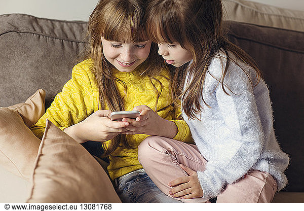 Sisters using phone on sofa at home