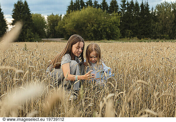 Sisters using smart phone amidst field