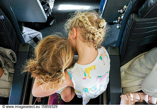 sisters walking through airplane aisle towards seat hugging