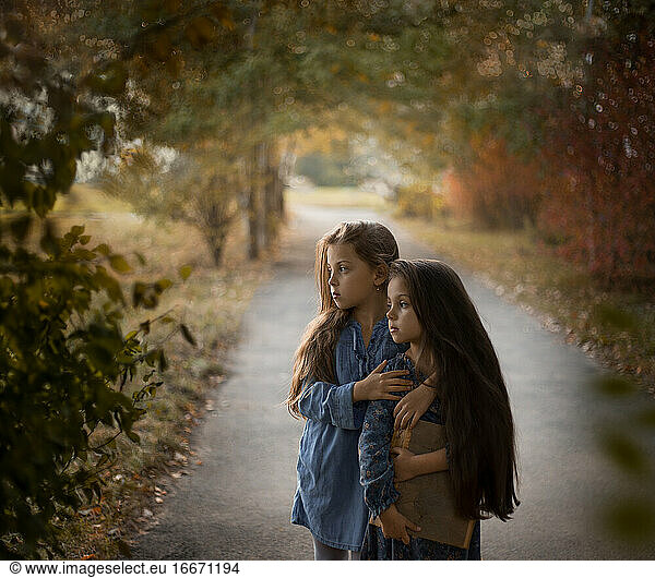 Sisters with a family album in their hands stand in the fall in nature