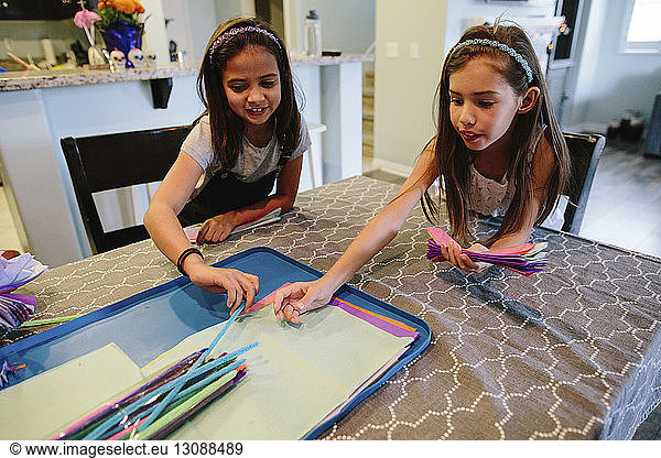 Sisters with colorful papers taking sweet candies while sitting at table