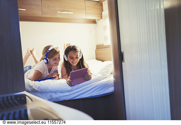 Sisters with headphones sharing digital tablet  watching video inside motor home