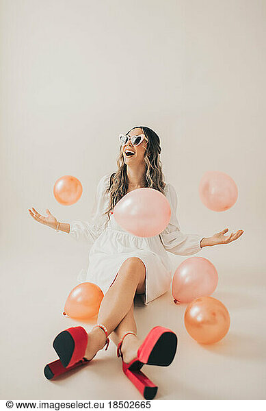 Sitting Woman Laughing and Tossing Pink Balloons in Air