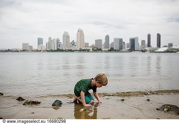 Six Year Old Boy Kneeling in Bay San Diego Skyline in Background