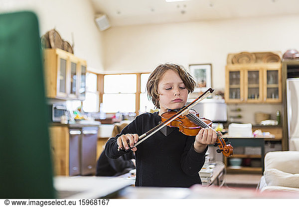Six year old boy playing violin  having a remote video lesson in lockdown at home.