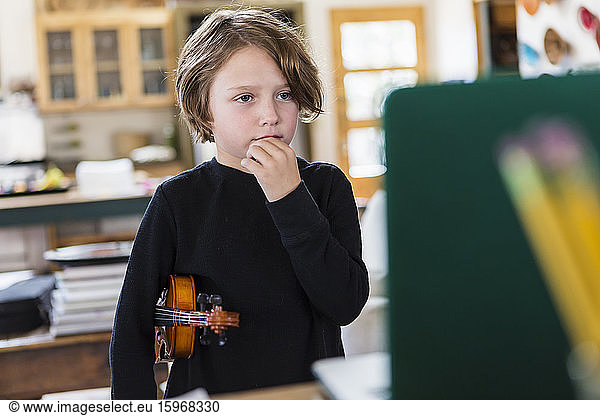 Six year old boy playing violin  having a remote video lesson in lockdown at home.