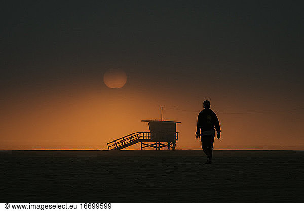 Skateboarder Walking Towards Moody Sunset in Venice Beach  CA USA