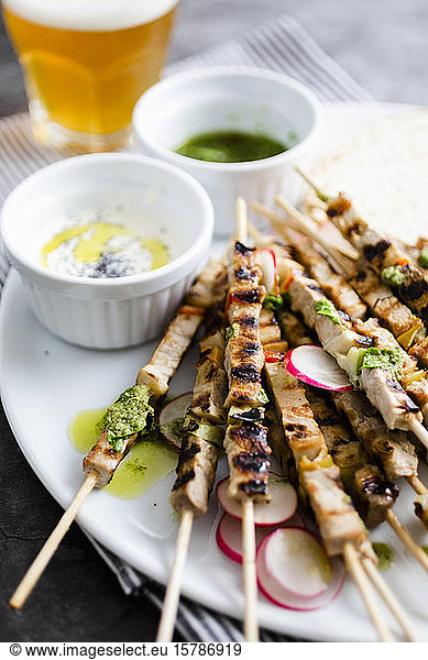 Skewers of meat on plate with yogurt and parsley sauce with flat bread and vegetables
