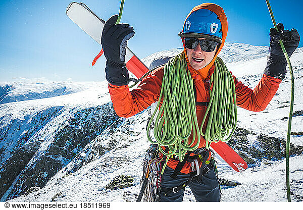 Ski mountaineer coiling rope with snowy mountains behind