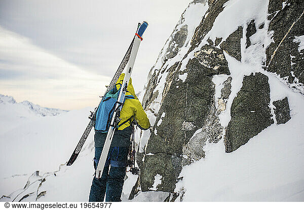 skier forced to bootpack skis to the summit due to cliffs and rocks