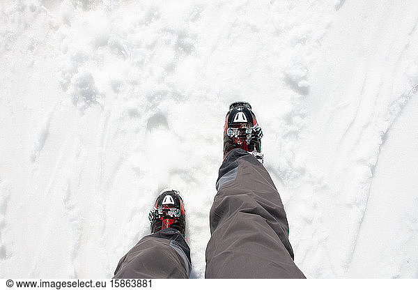 Skier legs with black pants and his red ski boots walking on snow