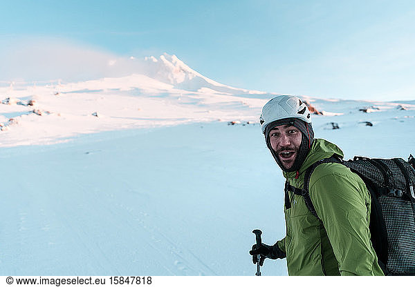 Skier looking at camera smiling while skinning up mountain