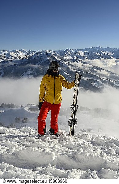 Skier standing at the ski slope holding ski  view into the distance  summit Hohe Salve  SkiWelt Wilder Kaiser Brixenthal  Hochbrixen  Tyrol  Austria  Europe