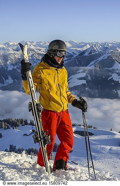 Skier stands at the ski slope and holds ski  in front of mountain panorama  summit Hohe Salve  SkiWelt Wilder Kaiser Brixenthal  Hochbrixen  Tyrol  Austria  Europe
