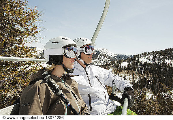 Skiers looking away while sitting in ski lift against clear sky
