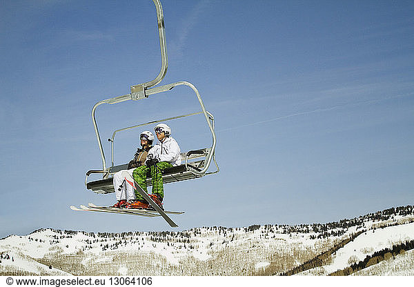 Skiers sitting in ski lift against clear sky