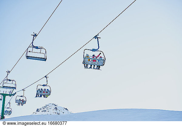 Skifahrer auf einem Sessellift mit Blick nach unten und blauem Hintergrund