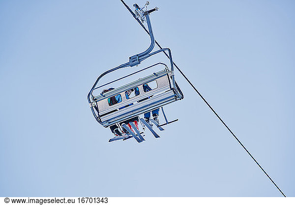Skifahrer auf einem Sessellift mit Blick nach unten und blauem Hintergrund