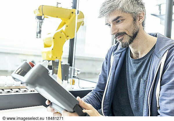 Skilled worker in robotic factory controlling robot arm with digital control