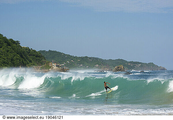 Skimboarder riding a turqoise wave in Mazunte  Oaxaca  Mexico.
